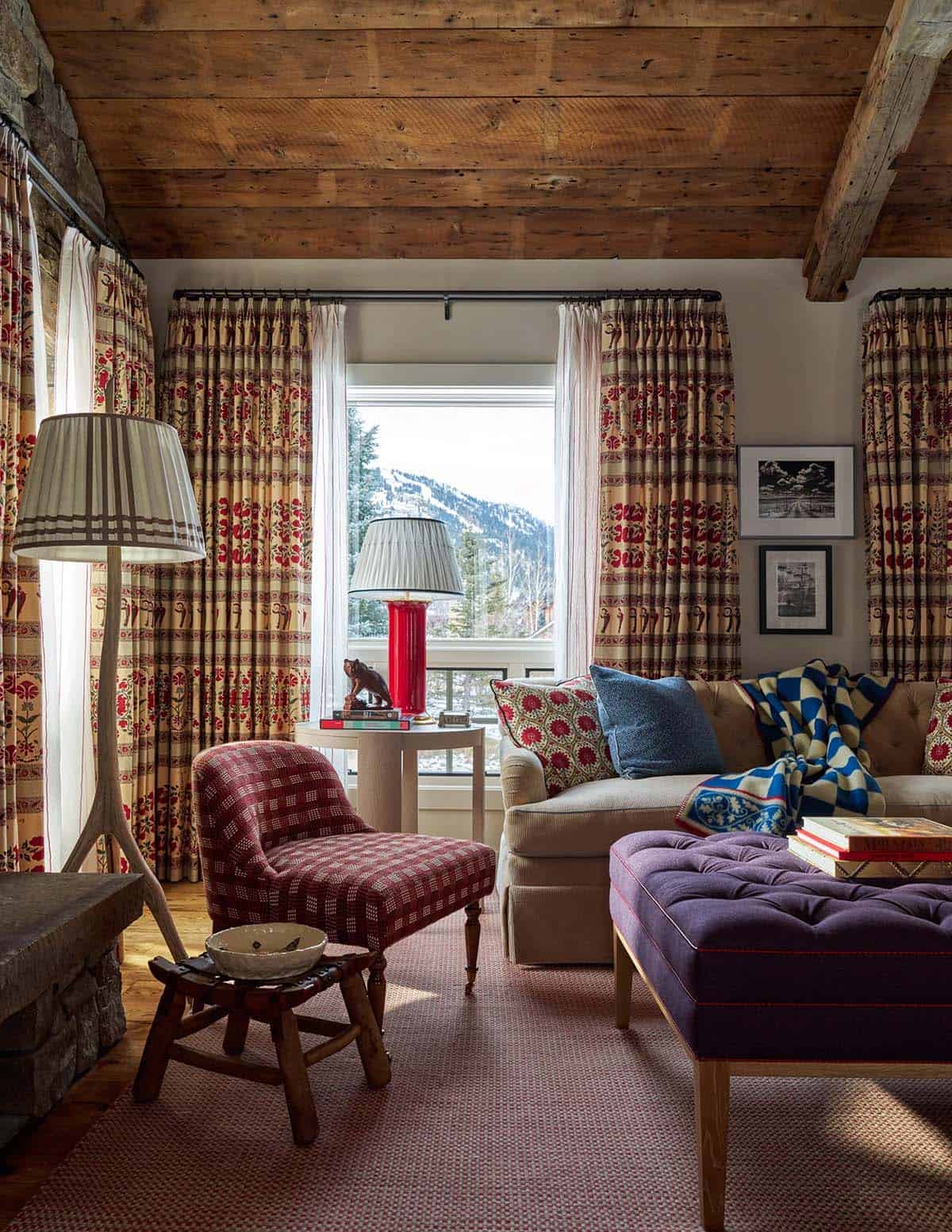 Family room with plaid armchair, tufted purple ottoman, patterned curtains, and snow-covered mountain view