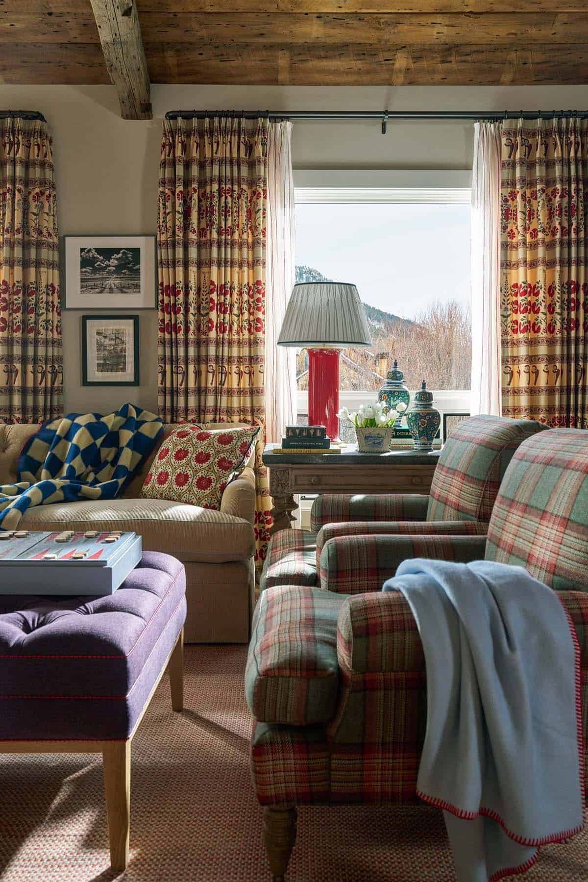 Family room detail with plaid armchairs, tufted purple ottoman, red lamp, and patterned curtains
