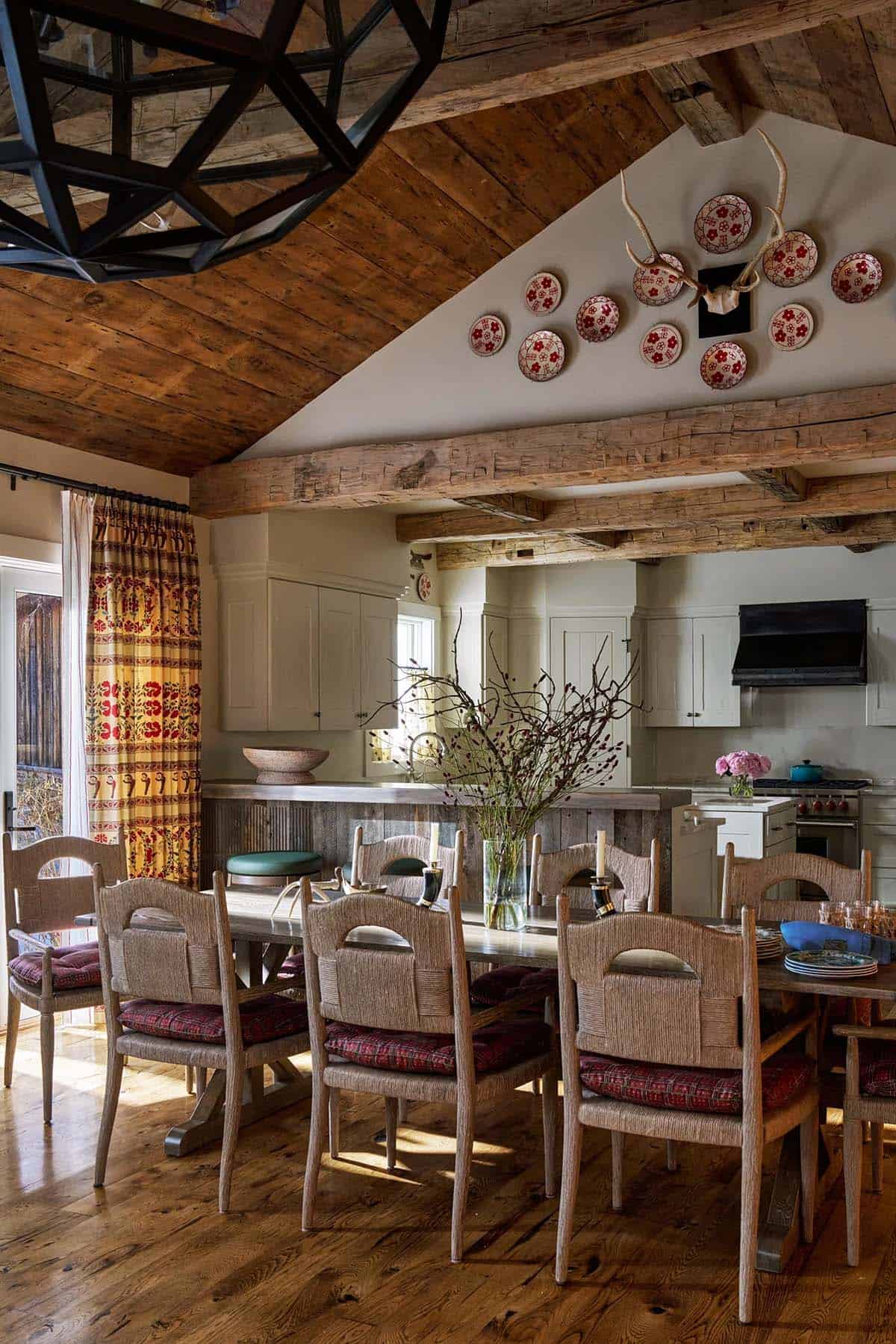 Open dining area with long table, rush chairs, vaulted timber ceiling, decorative plate wall, and kitchen beyond