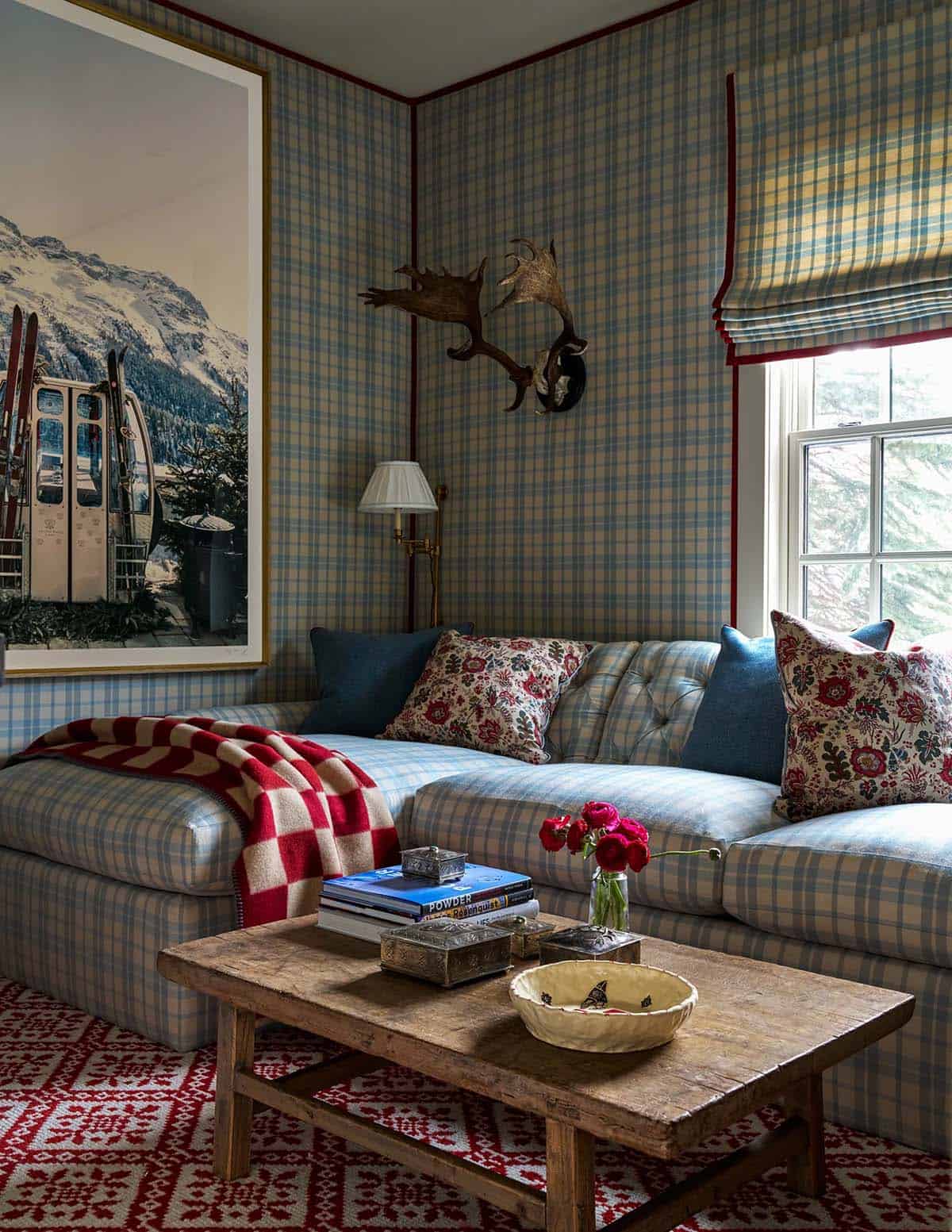 TV nook with plaid wallpaper sofa, red Nordic rug, antler mount, and large ski resort photograph