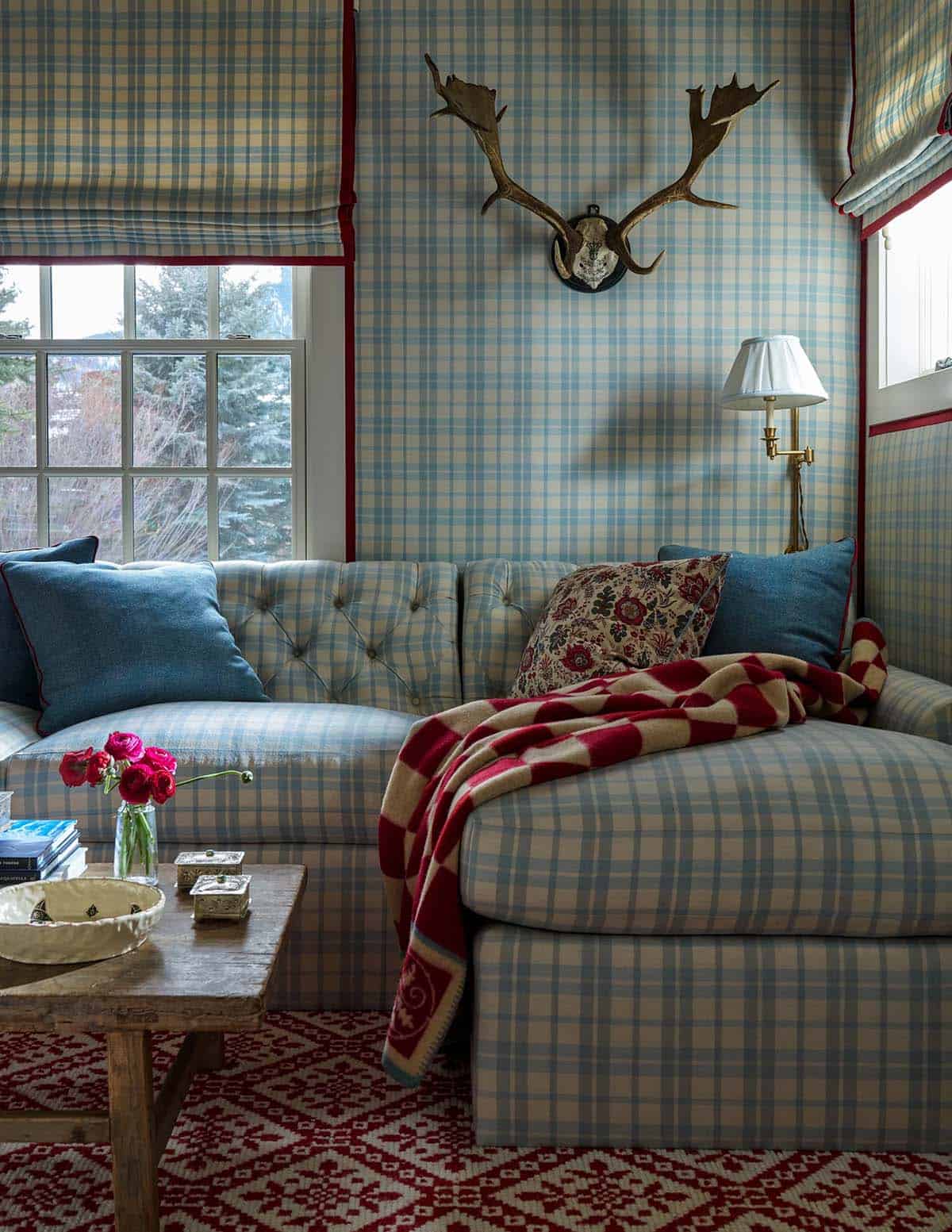 TV nook with floor-to-ceiling plaid fabric walls, tufted plaid sofa, antler mount, and red Nordic rug