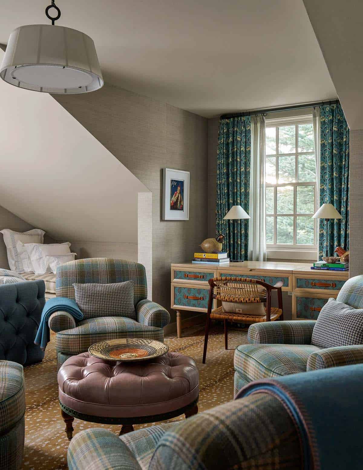 Bedroom sitting area with plaid armchairs, tufted leather ottoman, patterned desk, and teal floral curtains