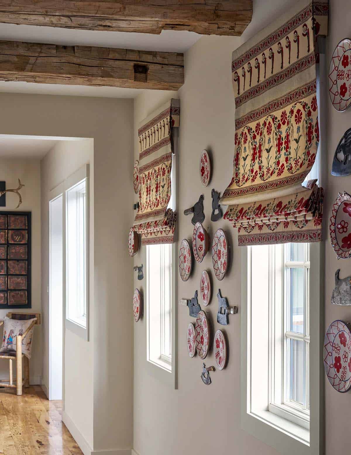 Hallway wall with collection of decorative folk art plates, vintage cleaver hooks, and patterned roman shades