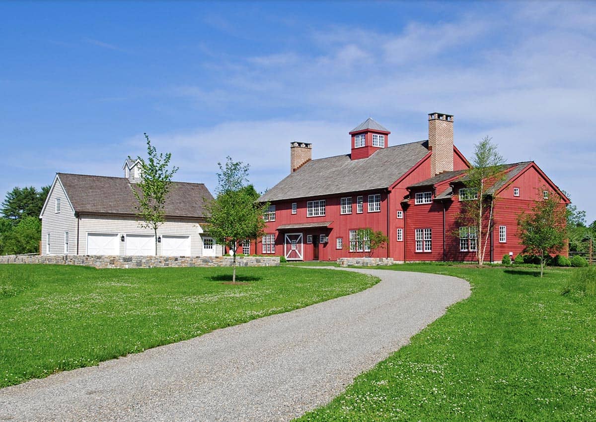 New England style red barn house exterior with gravel driveway and green lawn