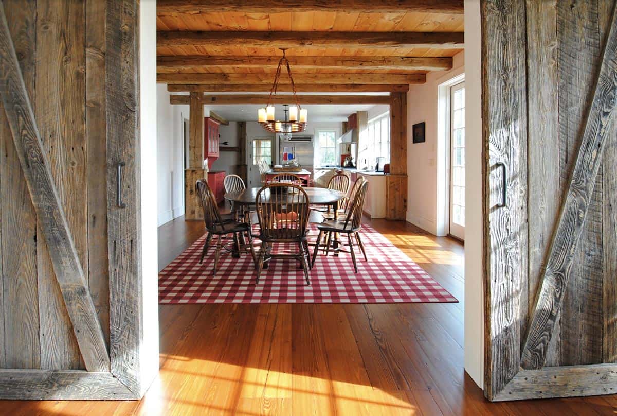 Dining room viewed through open reclaimed wood sliding barn doors with red plaid rug and Windsor chairs