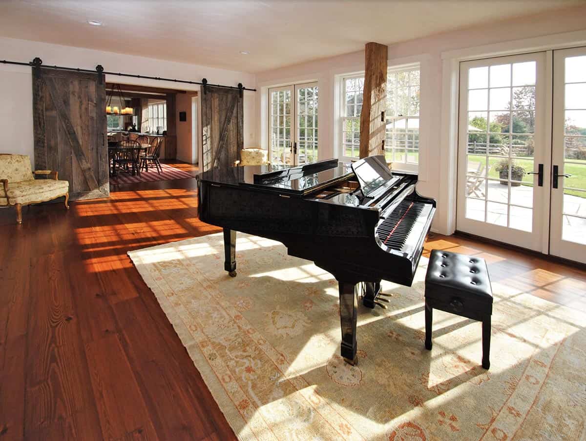 Bright living room with black grand piano, reclaimed wood beam, and sliding barn doors opening to dining area