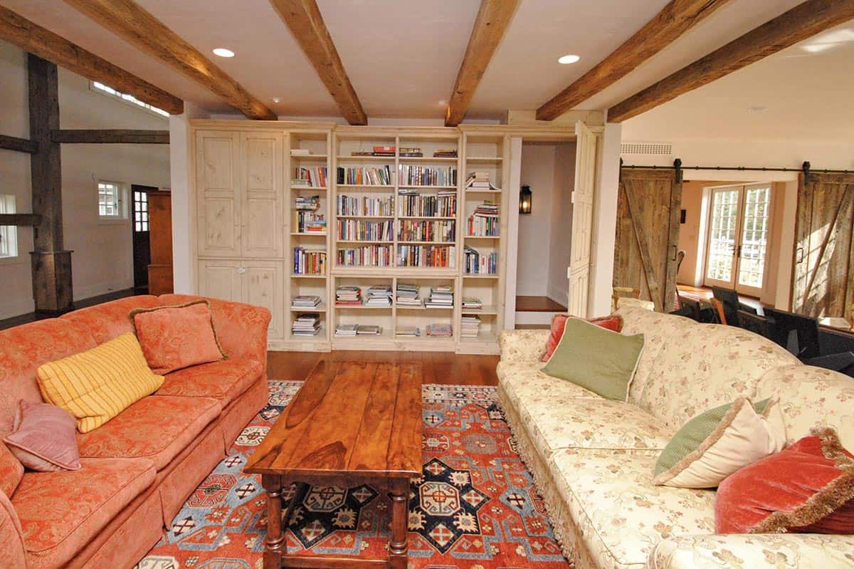 Cozy living room with exposed ceiling beams, built-in bookshelves, and two sofas around a wood coffee table