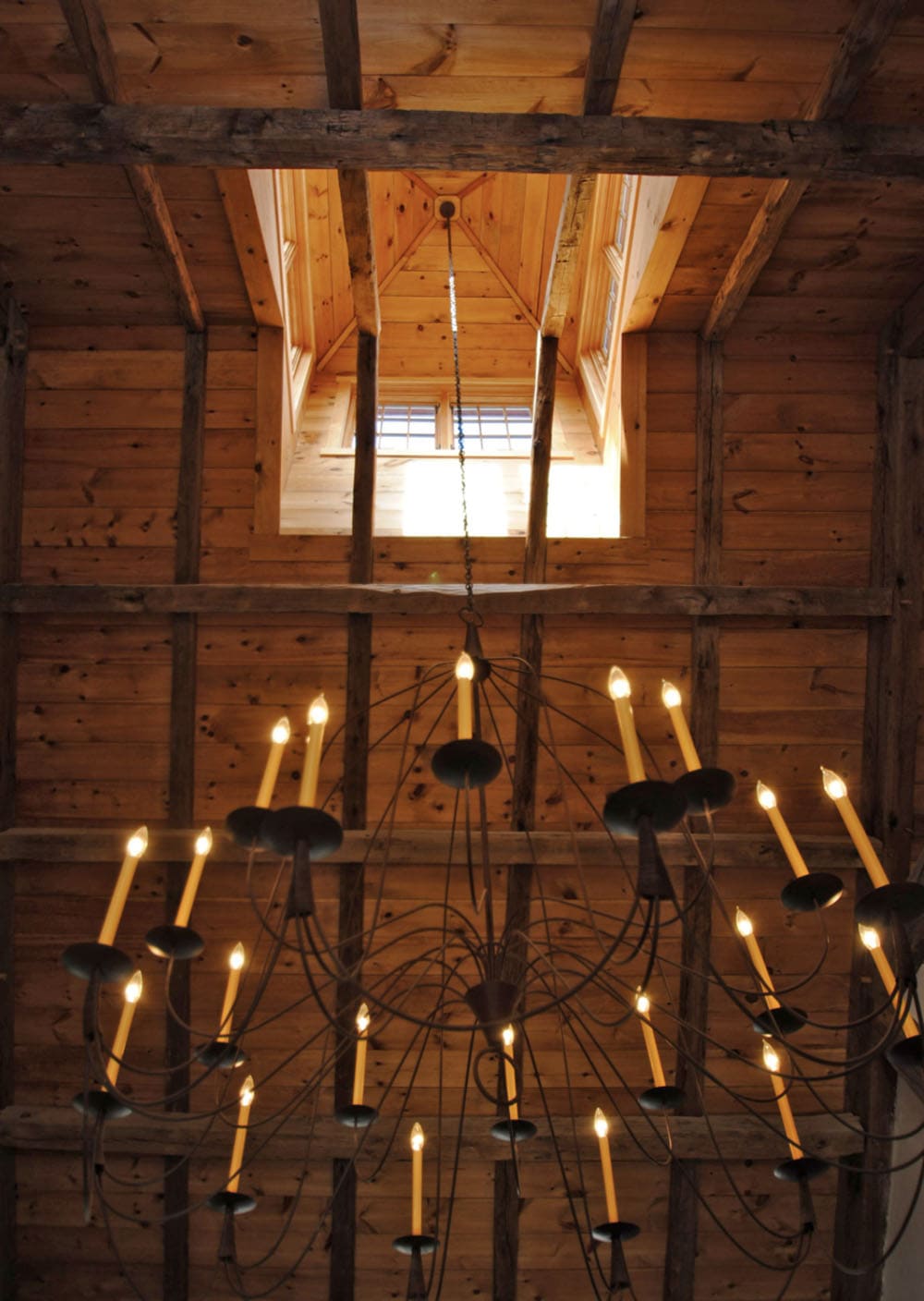 Upward view of wrought iron candle chandelier beneath exposed timber frame ceiling and cupola skylight