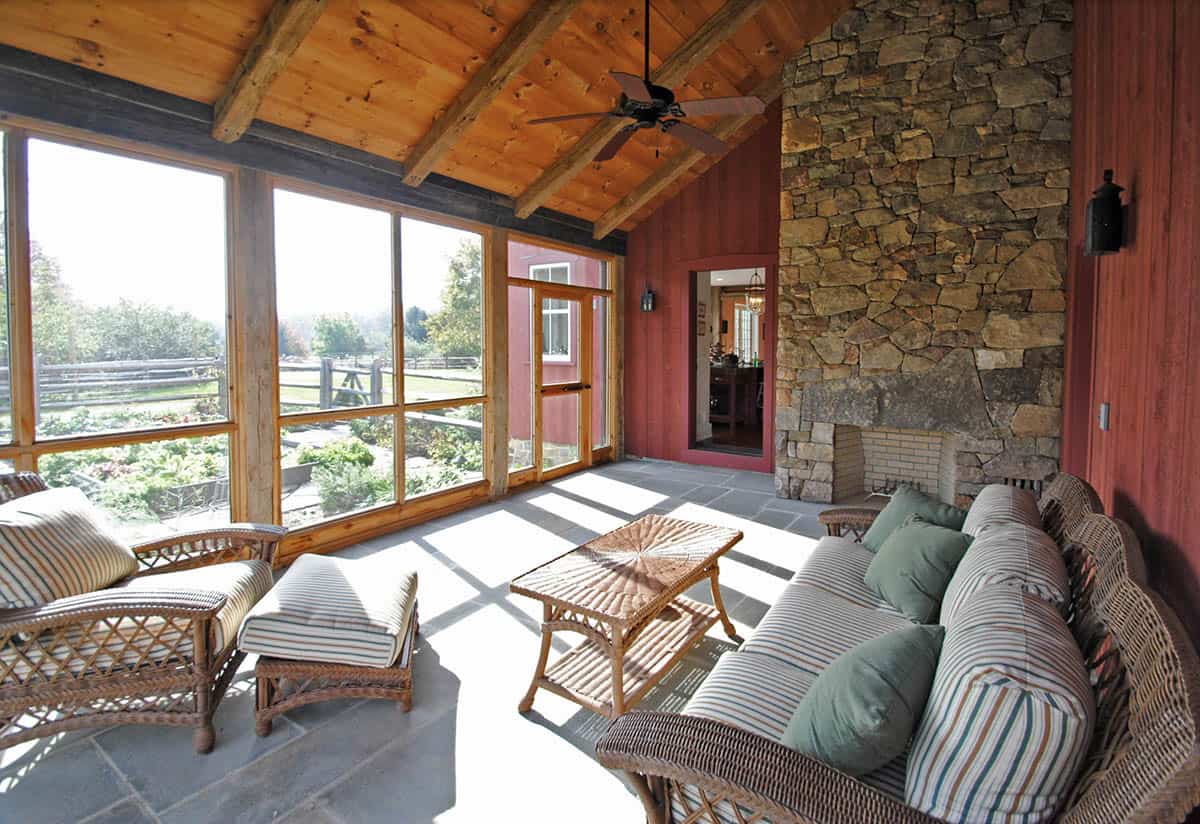 Screened porch with wicker furniture, stone fireplace wall, wood beam ceiling, and garden views