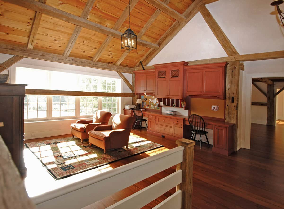 Loft sitting area with exposed timber frame ceiling, red built-in desk cabinetry, and mezzanine railing