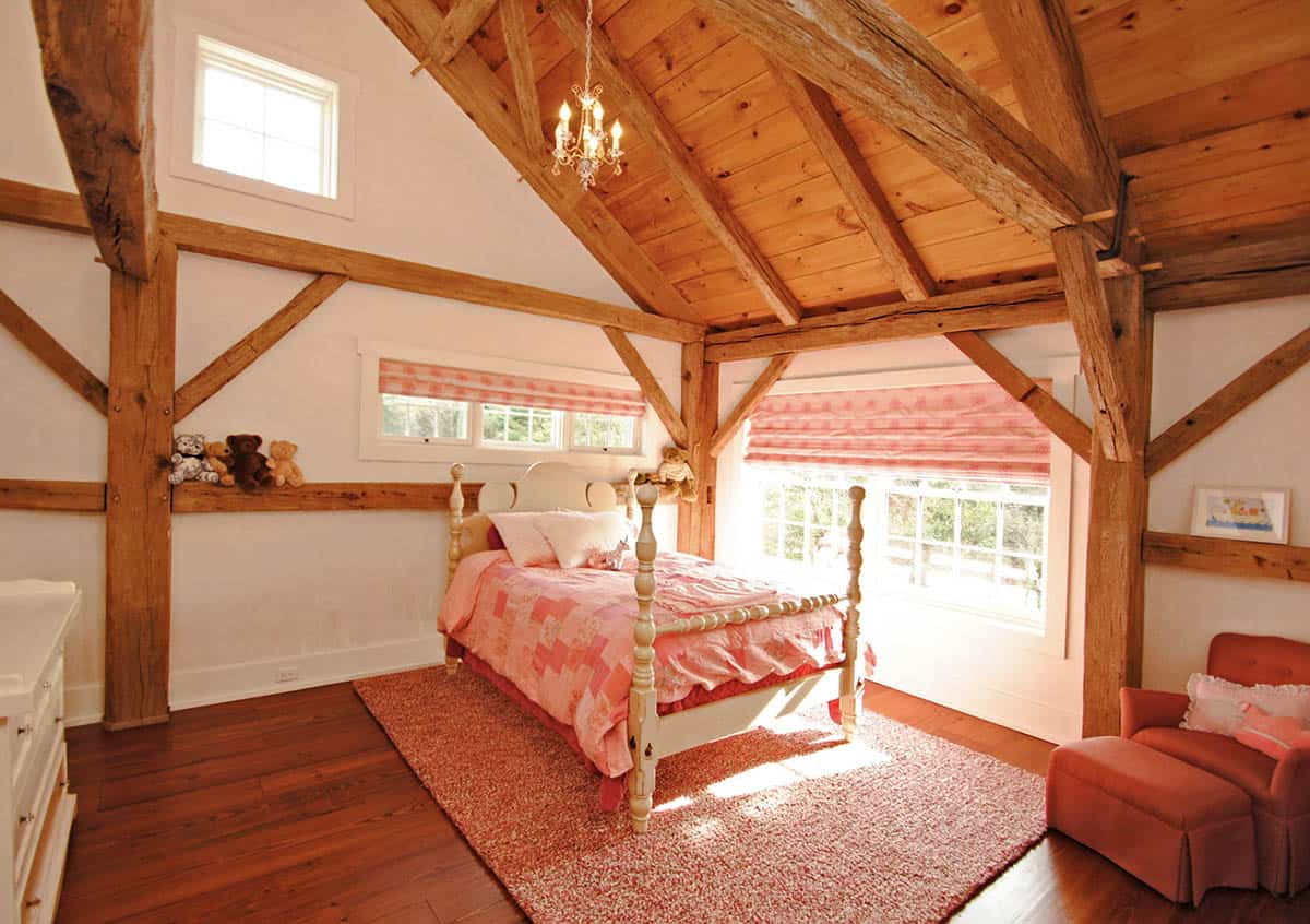 Girl's bedroom with exposed timber frame ceiling, white four-poster bed, pink bedding, and chandelier