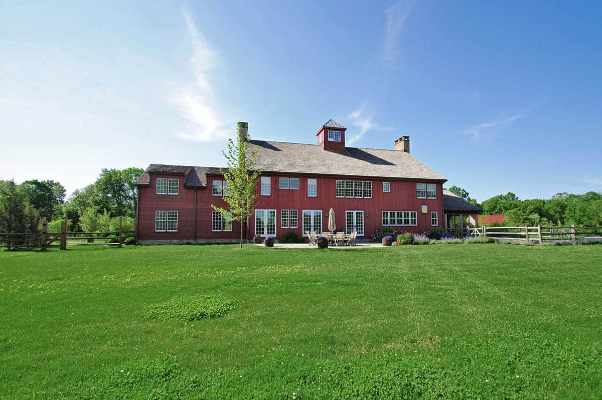 Rear exterior of red New England barn house with patio seating, cupola, and green lawn