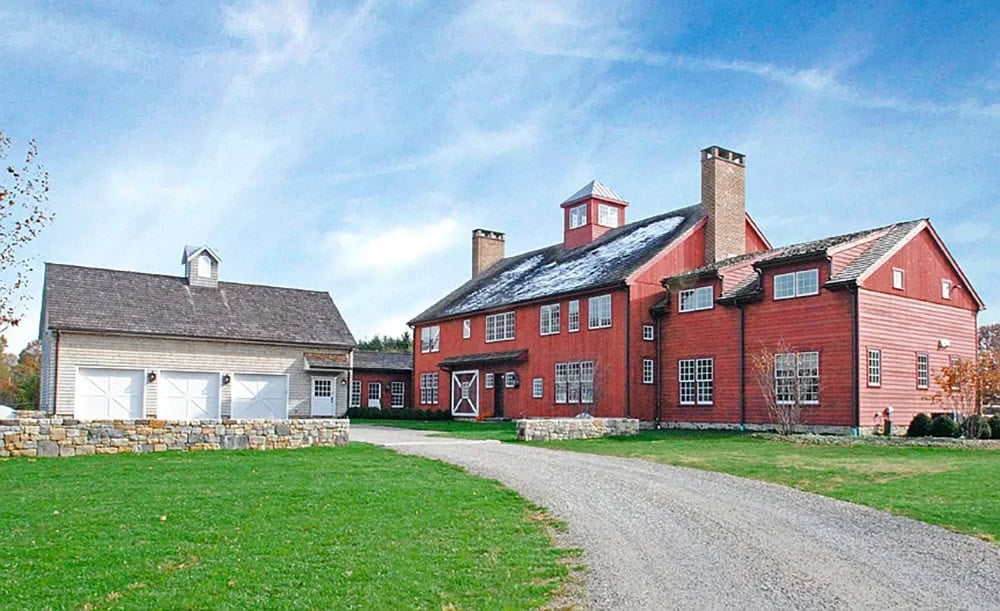 Front exterior of red New England barn house with white garage outbuilding in winter