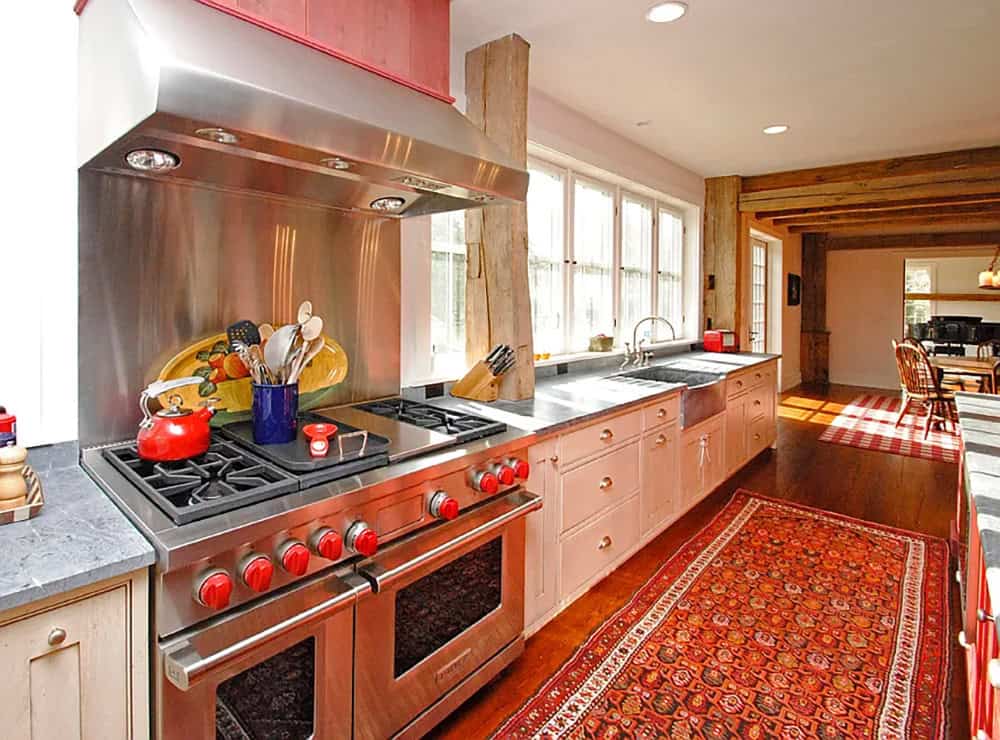 Farmhouse kitchen with professional stainless range, red knobs, stainless backsplash, and Persian runner