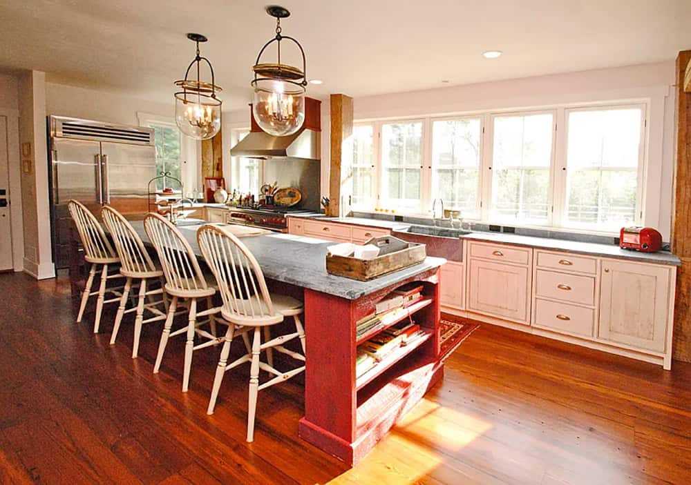 Farmhouse kitchen island with red base, soapstone countertop, Windsor barstools, and globe pendants
