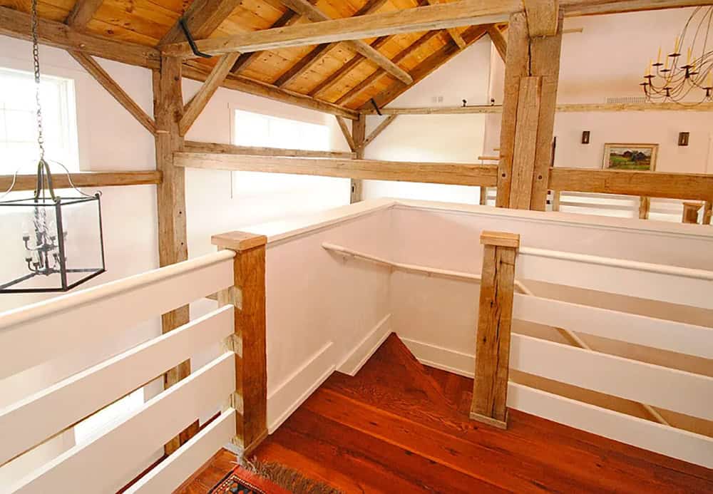 Mezzanine landing with white railings, exposed timber frame posts, and wood plank ceiling