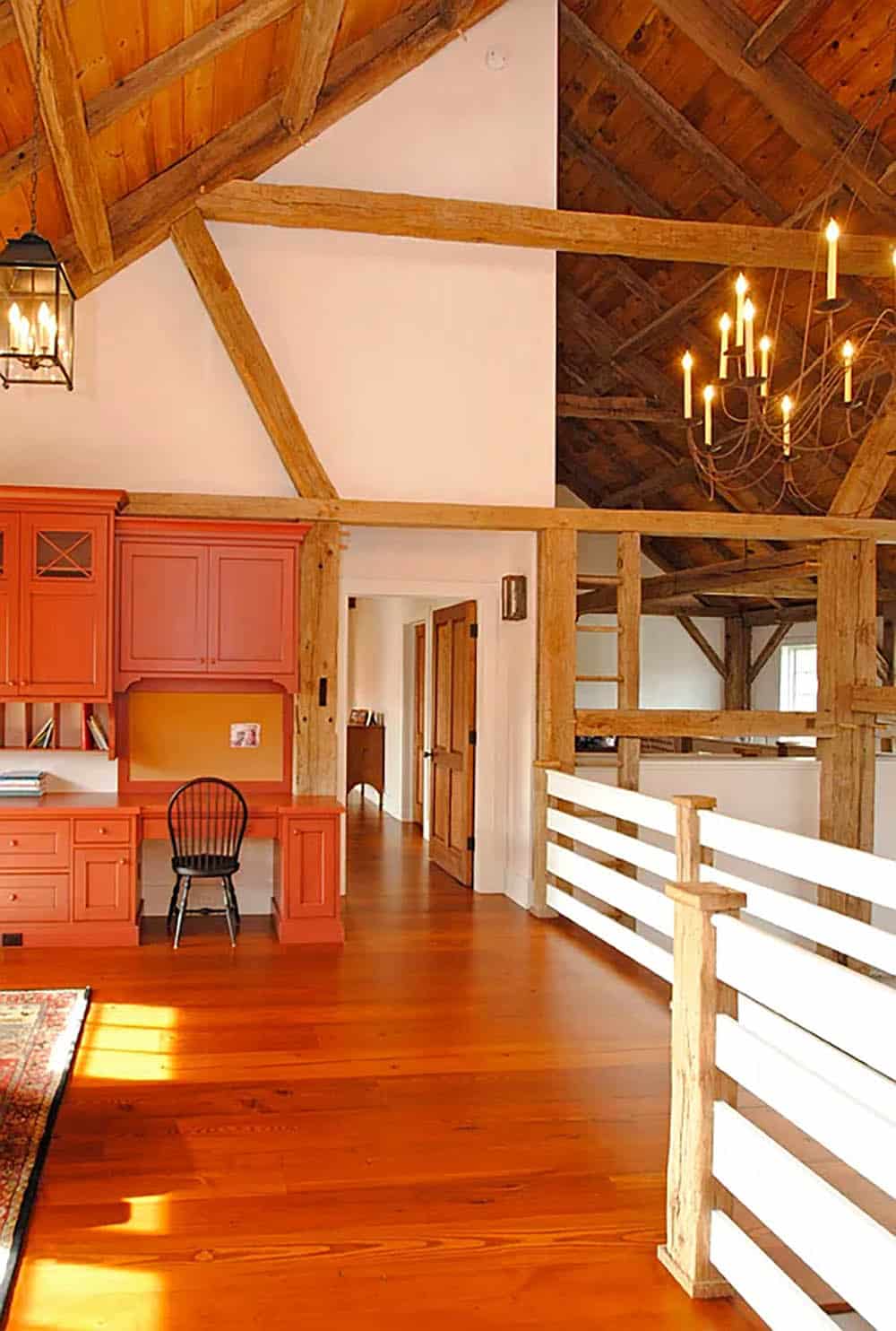 Upper loft hallway with red built-in desk, exposed timber frame ceiling, and white mezzanine railing