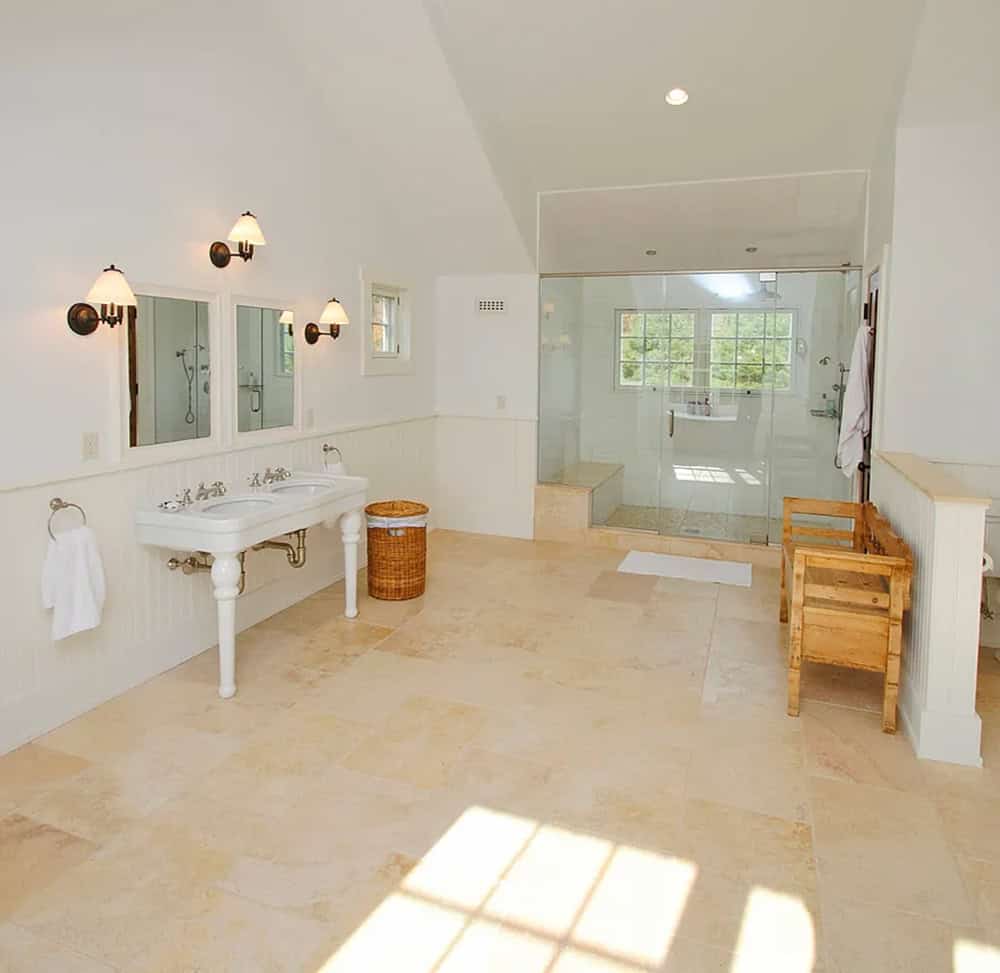 Spacious white master bathroom with double pedestal sink, glass walk-in shower, and travertine tile floor