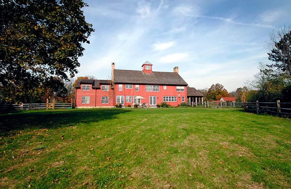 Rear exterior of red New England barn house with cupola, split rail fence, and autumn landscape