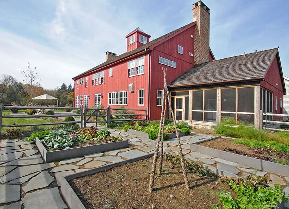 Raised bed kitchen garden with flagstone paths beside red barn house screened porch