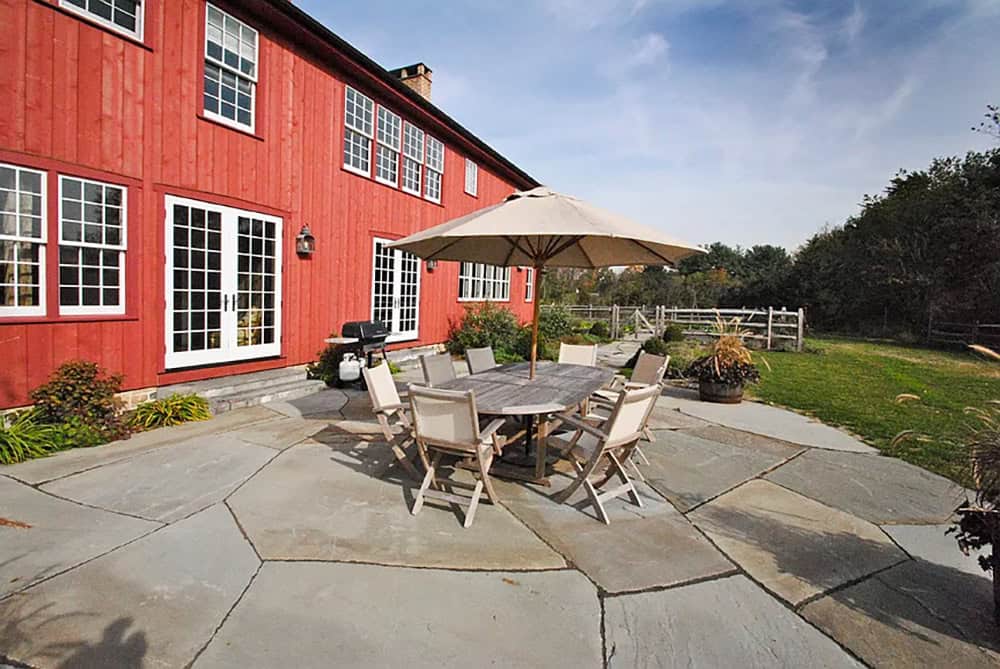 Bluestone patio with teak dining set and umbrella alongside red barn house French doors