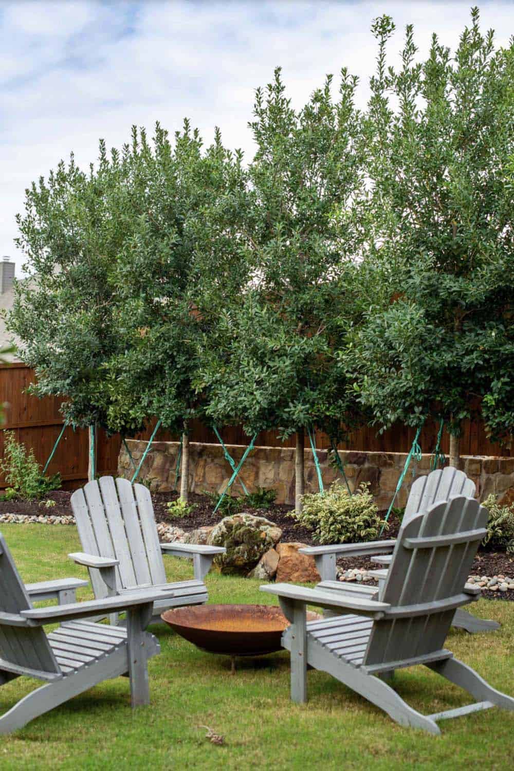 Backyard fire pit seating area with row of trees as natural privacy screen