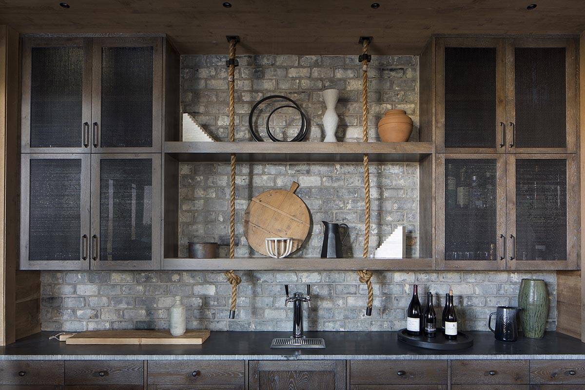 Close-up of barn bar with rope-hung shelves, brick backsplash and wine tap