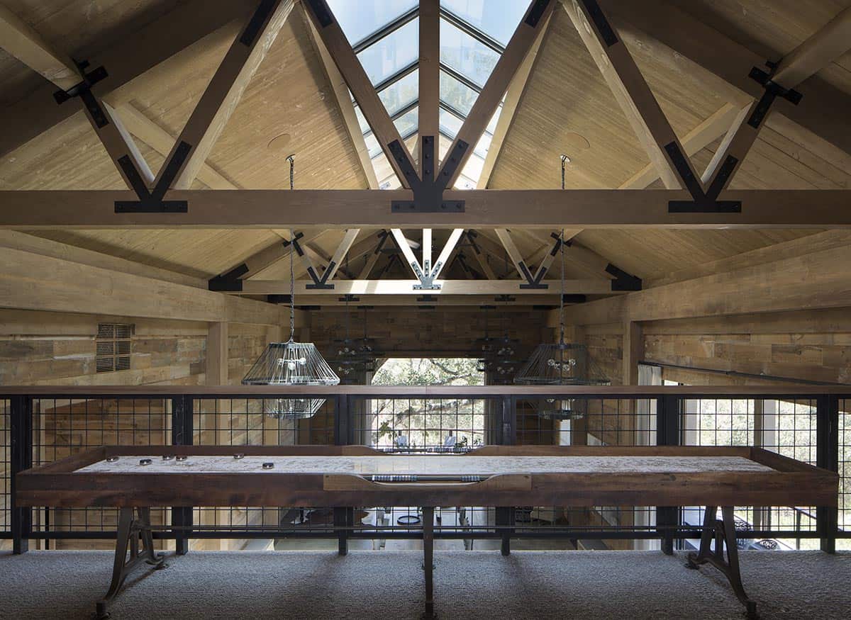 Mezzanine shuffleboard table beneath skylit timber roof trusses overlooking main hall