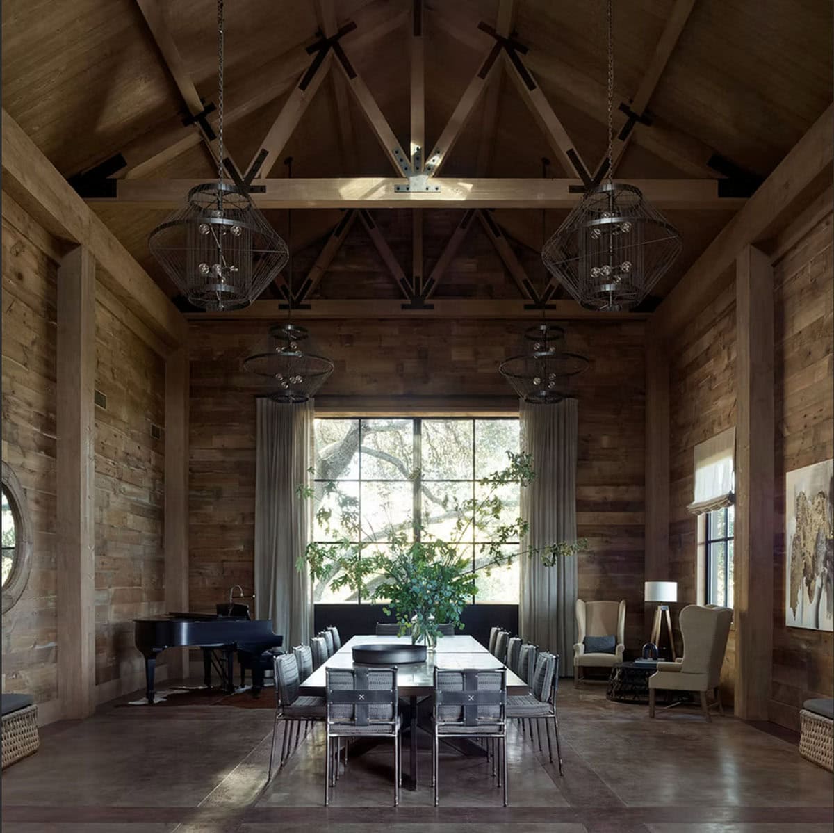 Dramatic barn dining hall with timber trusses, cage pendants and grand piano
