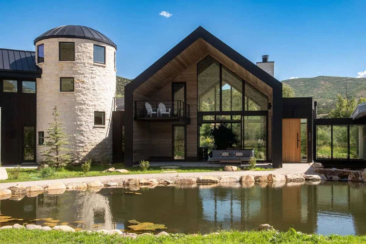 Stone-clad silo and dark wood barn wing reflected in a trout pond, Brighton Architectural Group ranch, Utah