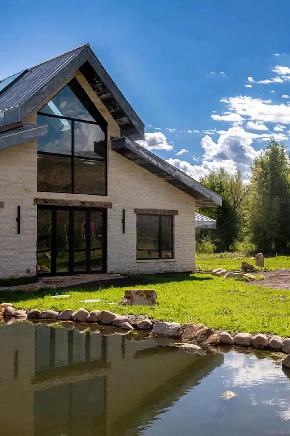 White limestone wing with gabled roofline and black-framed windows reflected in a pond, Park City ranch