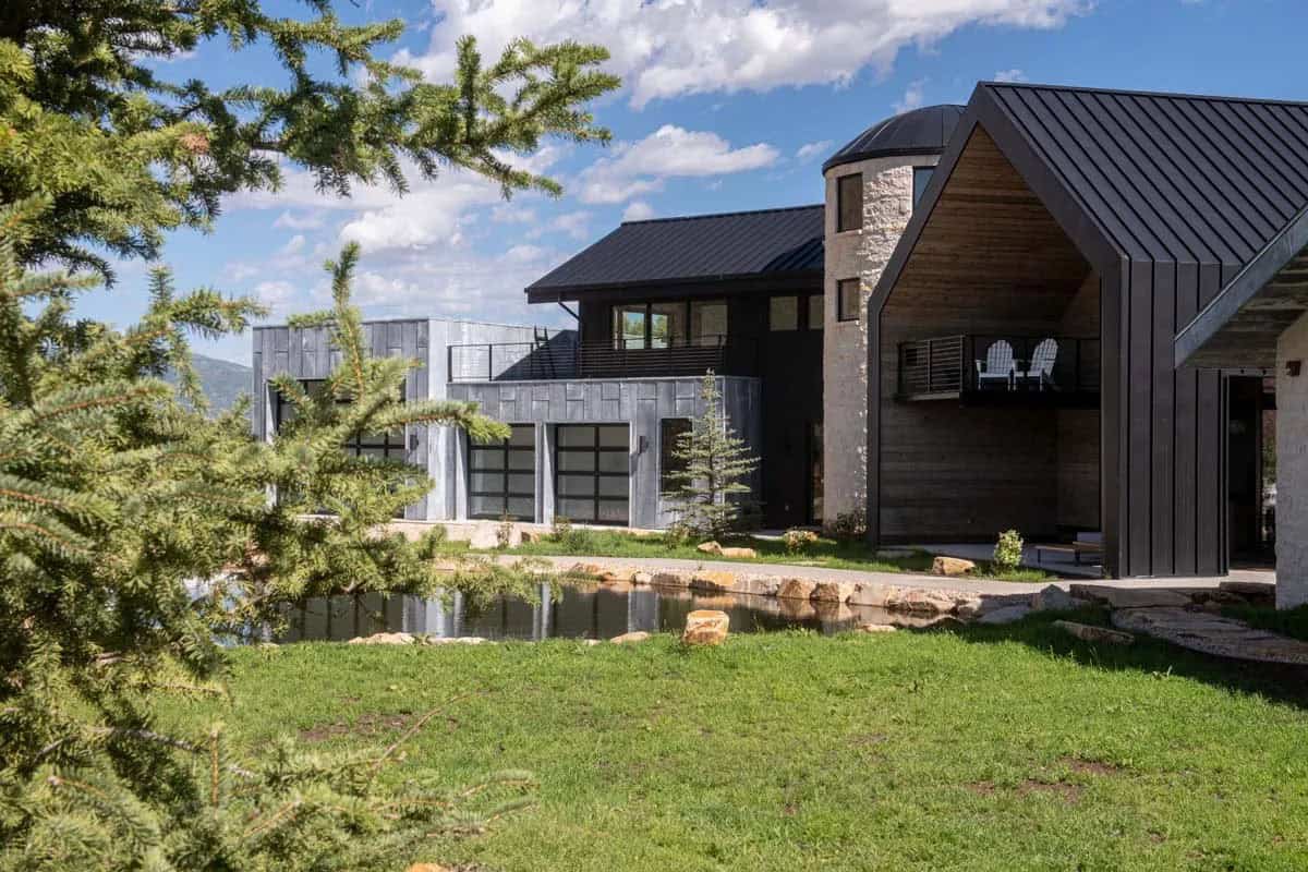 Rear view of ranch compound through pine trees with stone silo and wood-clad barn structure, Park City