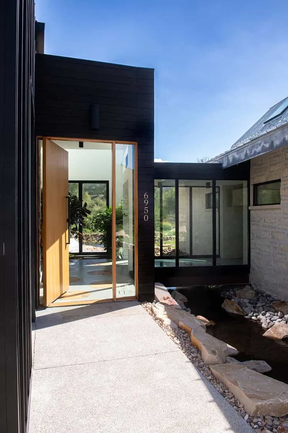 Warm wood pivot entry door flanked by black steel framing with stream running alongside the entrance