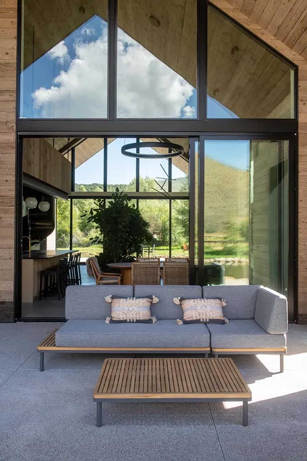 Outdoor lounge seating area with teak coffee table facing floor-to-ceiling glazing and mountain views