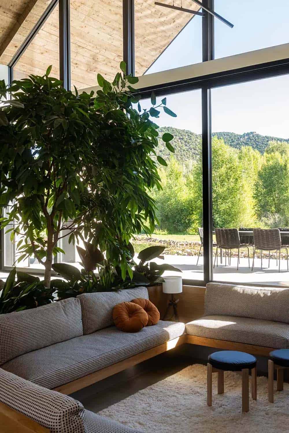 Sunken living room with built-in bench seating, oversized indoor plants, and floor-to-ceiling mountain views