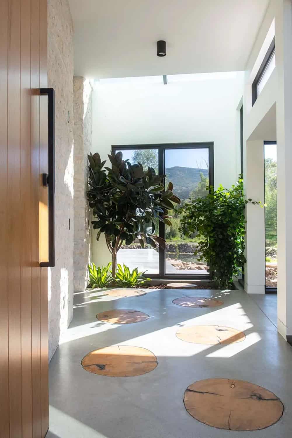 Light-filled foyer with polished concrete floor inlaid with live-edge wood rounds and lush indoor greenery
