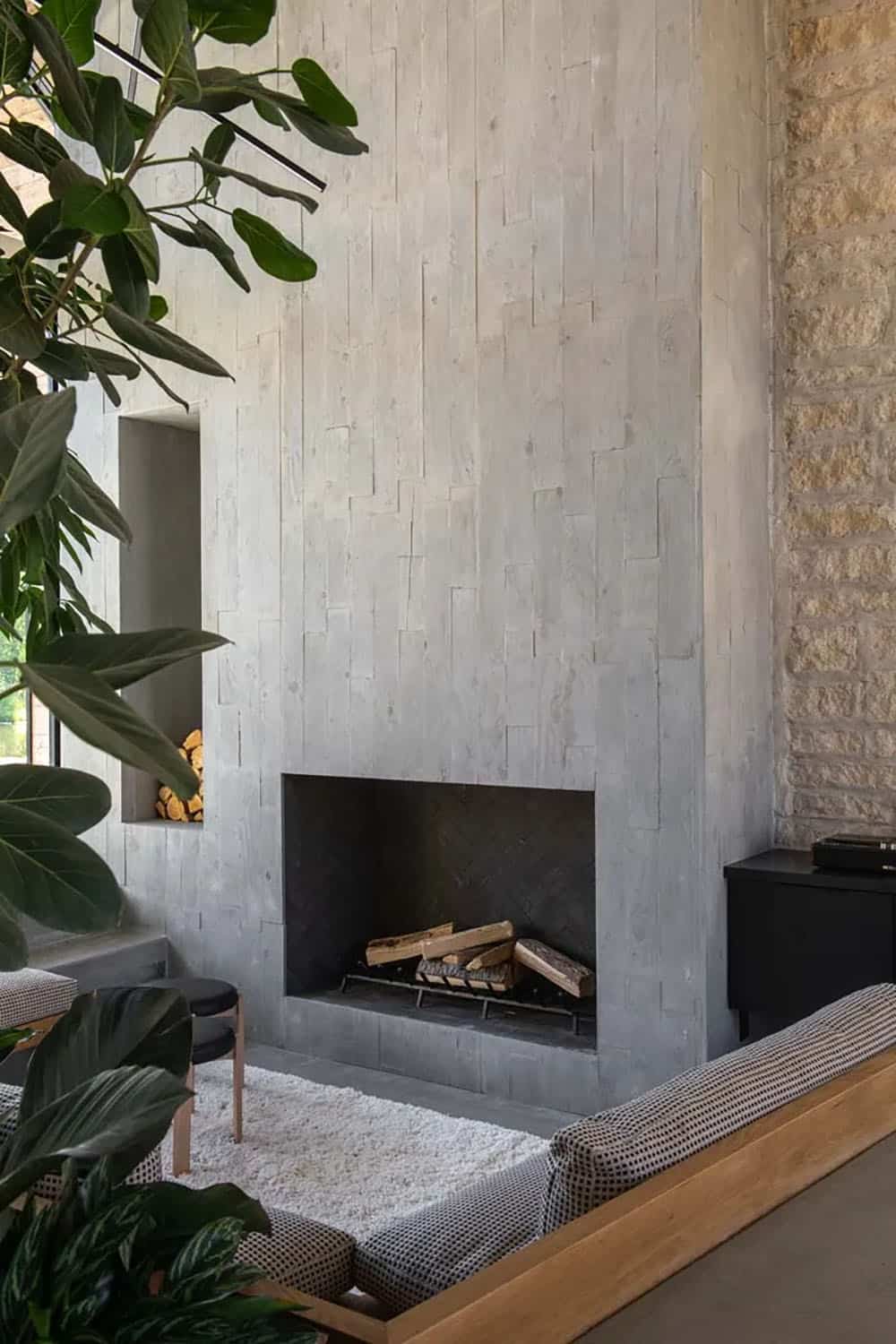 Soaring concrete-clad fireplace in sunken living room with built-in wood bench seating and stone accent wall