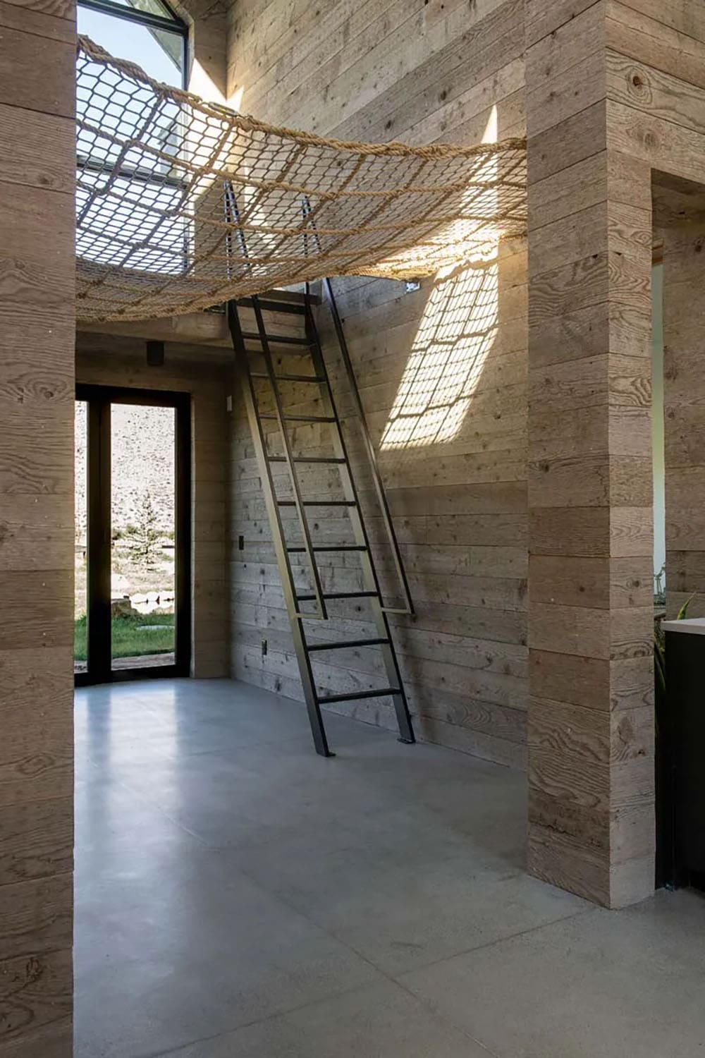 Reclaimed wood-clad room with steel ladder leading to rope net loft, contemporary ranch interior