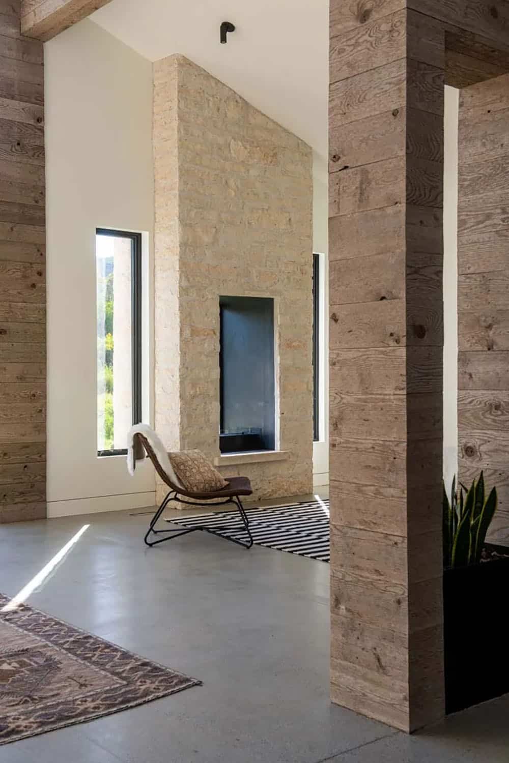 Stone fireplace with linear firebox and leather lounge chair in light-filled room with reclaimed wood columns