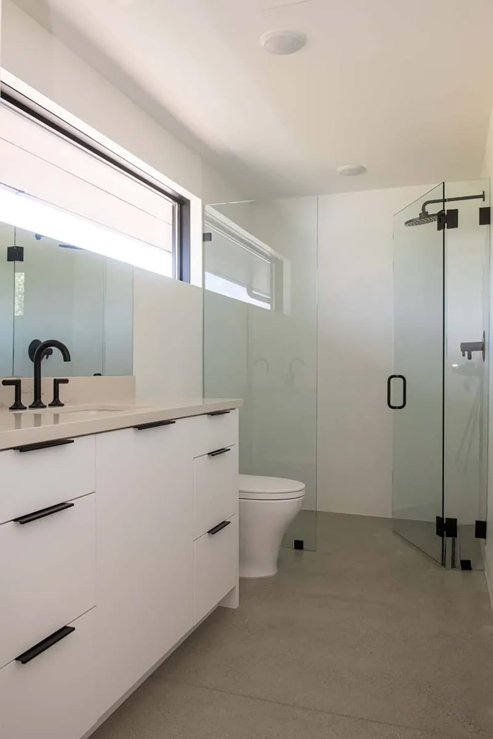 Clean white bathroom with matte black fixtures, frameless glass shower, and concrete floor, Park City ranch