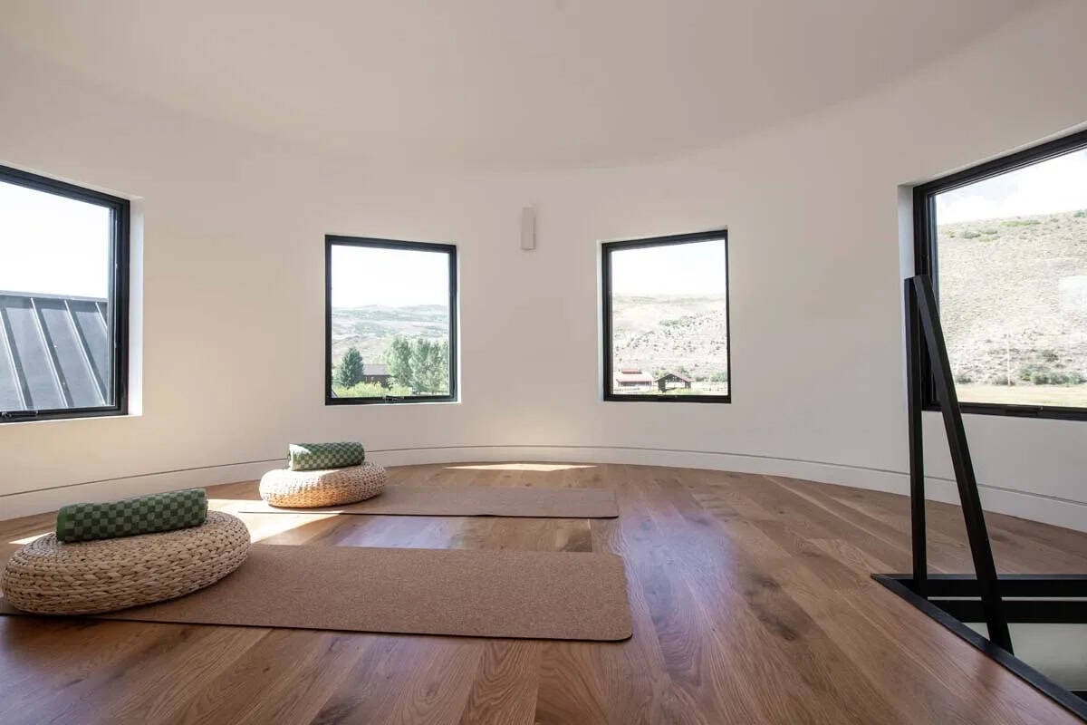 Circular yoga studio inside stone silo with warm wood floors, yoga mats, and panoramic Wasatch mountain views