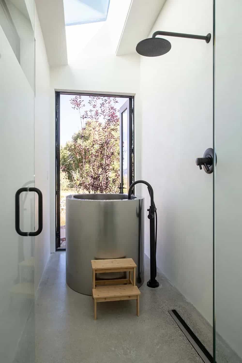 Japanese-style stainless soaking tub with floor-to-ceiling window, skylight, and matte black rain shower