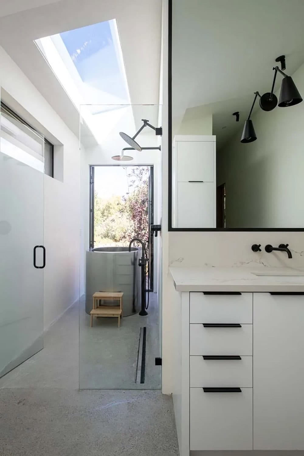 Primary bathroom with white vanity, black wall-mount faucet, frosted glass shower, and skylight above soaking tub