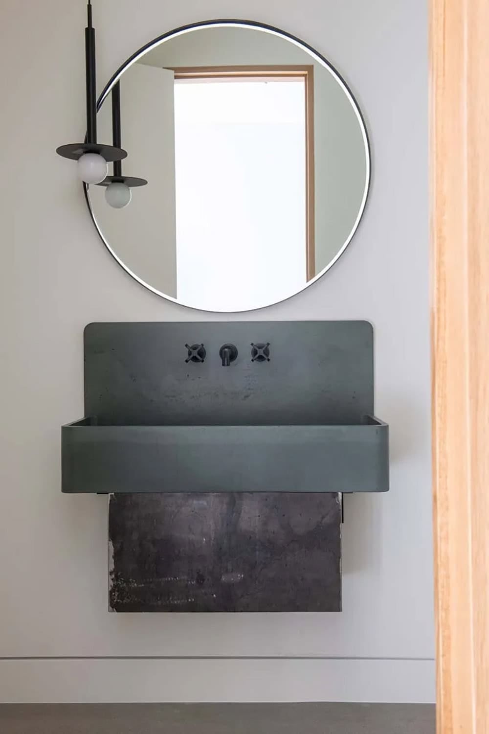 Sculptural concrete trough sink with matte black cross-handle faucet and round mirror, contemporary powder room