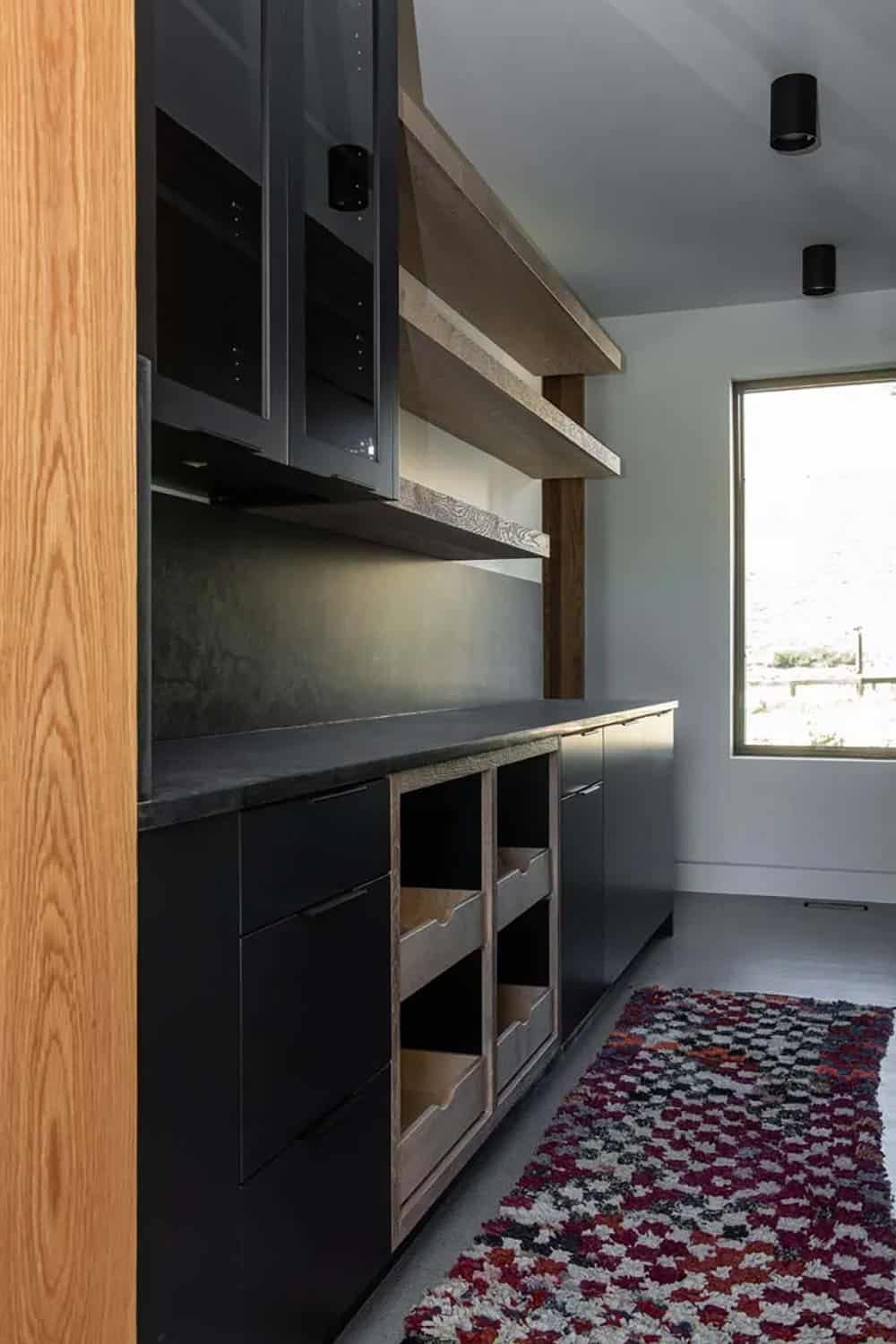 Dark butler's pantry with matte black cabinetry, open wine storage, reclaimed wood shelving, and colorful Moroccan runner