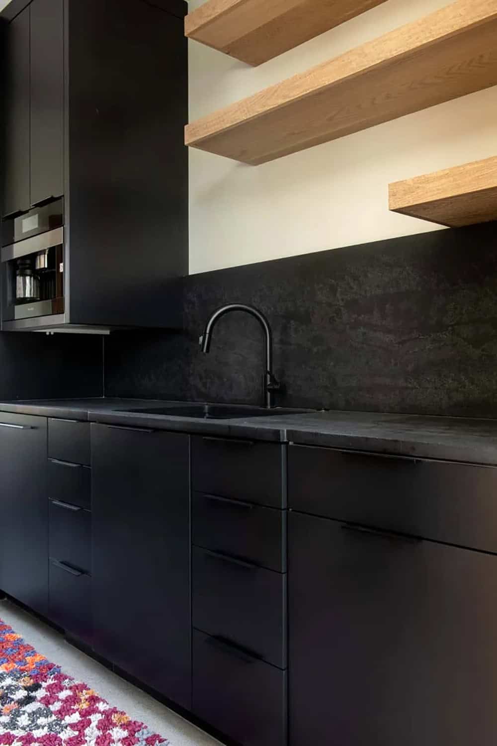 All-black kitchen perimeter with matte stone countertops, built-in appliances, and natural oak floating shelves