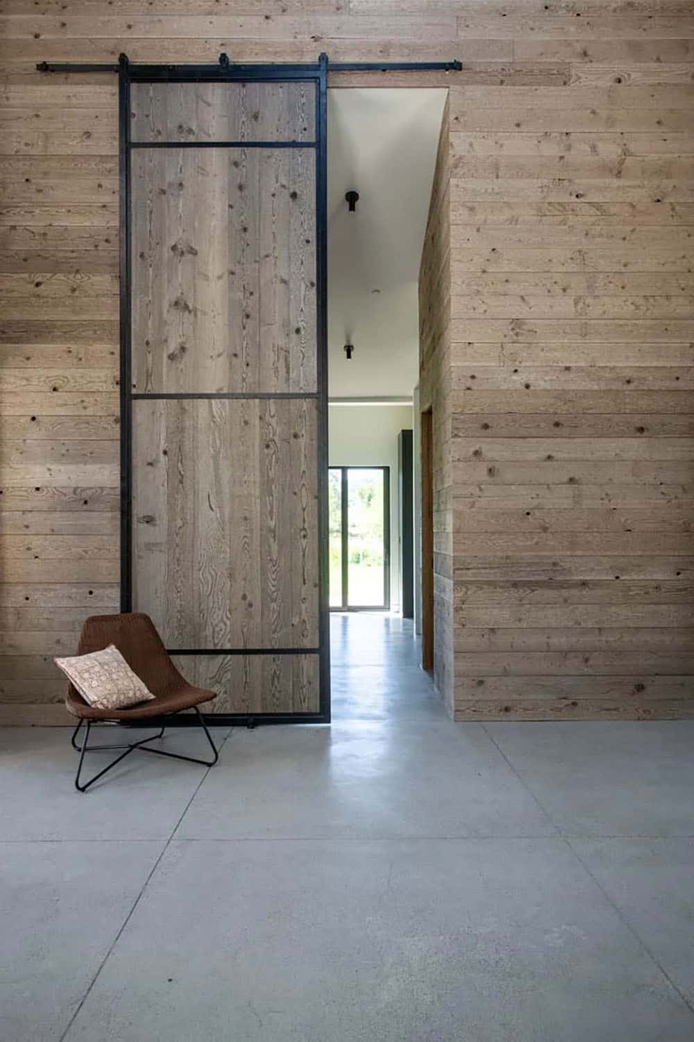 Oversized reclaimed wood sliding barn door with black steel frame on floor-to-ceiling wood-clad wall