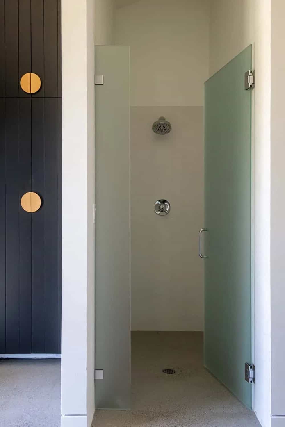 Minimal walk-in shower with frosted glass door, rain showerhead, and black vertical-board cabinet with wood pulls