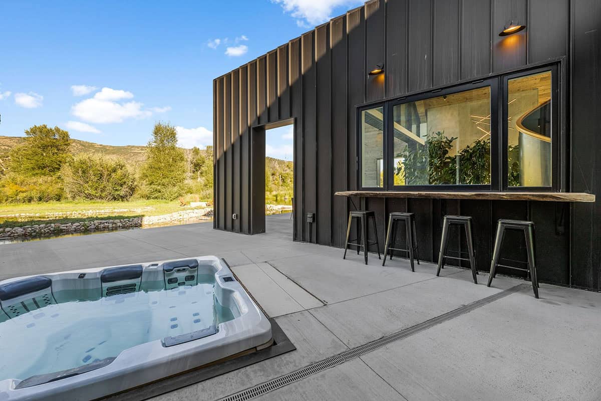Sunken hot tub on concrete patio beside dark steel barn exterior with outdoor bar