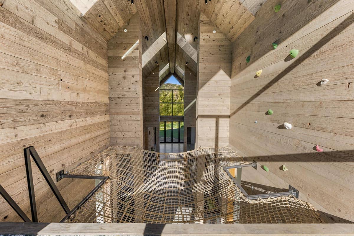 Indoor rock climbing wall and rope net hammock in a vaulted wood-clad adventure room